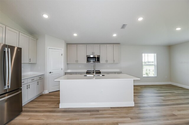 kitchen featuring recessed lighting, light countertops, appliances with stainless steel finishes, light wood-style floors, and a kitchen island with sink