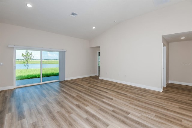 unfurnished room with baseboards, visible vents, a water view, and light wood finished floors