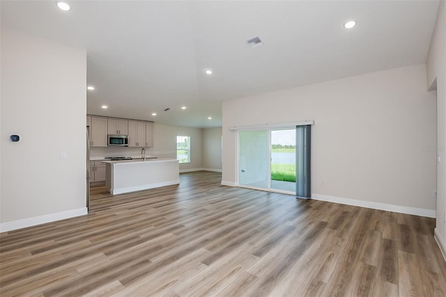 unfurnished living room with recessed lighting, visible vents, light wood-style flooring, a sink, and baseboards