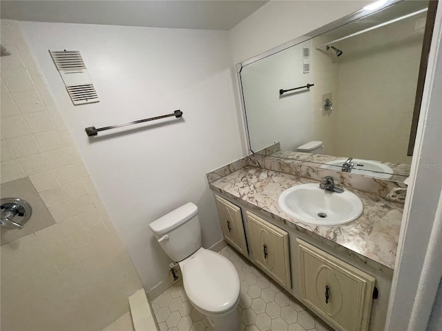 bathroom featuring toilet, vanity, tiled shower, and tile patterned floors