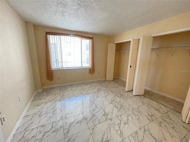 unfurnished bedroom with a textured ceiling and two closets