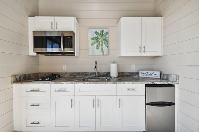 kitchen featuring white cabinetry, sink, stainless steel appliances, and wood walls