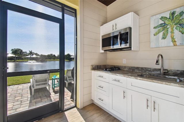 kitchen featuring a water view, white cabinetry, wooden walls, and sink