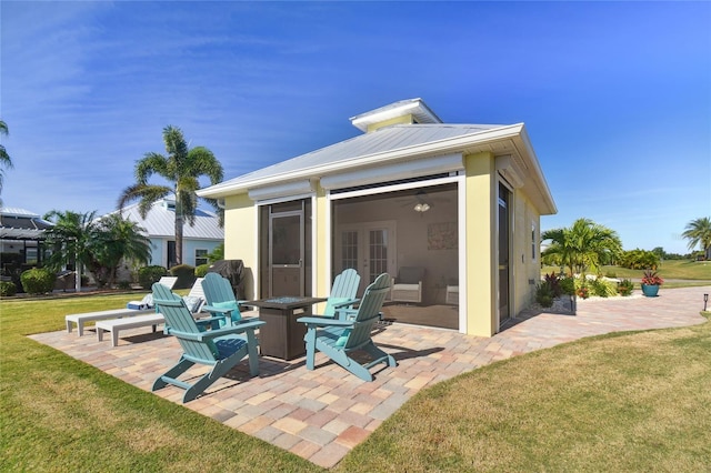 back of property with a sunroom, a yard, a patio, and an outdoor fire pit