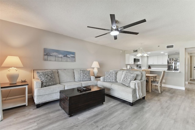 living room featuring ceiling fan with notable chandelier, light wood-type flooring, and a textured ceiling