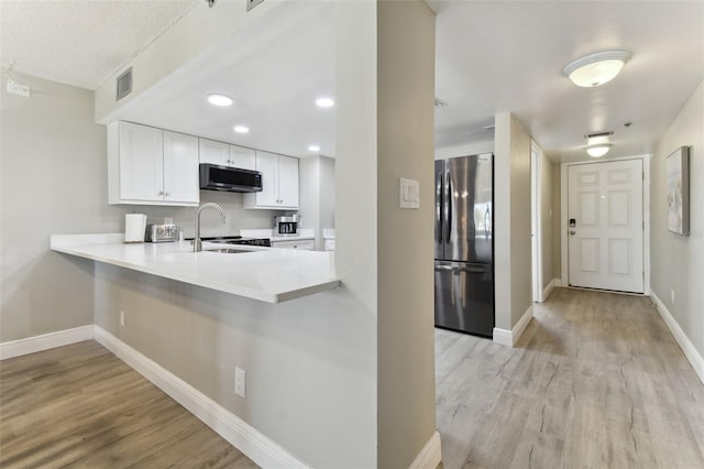 kitchen with sink, stainless steel appliances, kitchen peninsula, white cabinets, and light wood-type flooring