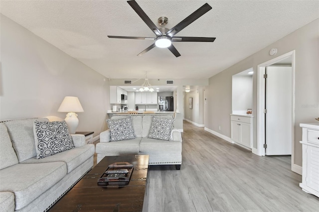 living room with ceiling fan with notable chandelier, light hardwood / wood-style floors, and a textured ceiling