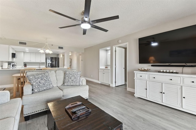 living room with ceiling fan with notable chandelier, a textured ceiling, and light hardwood / wood-style flooring