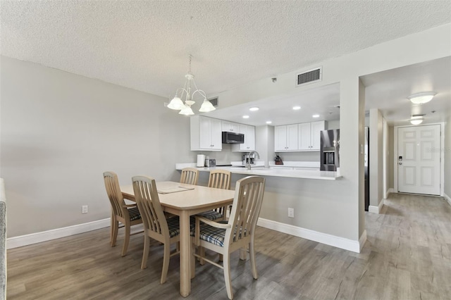 dining area featuring sink, wood-type flooring, a textured ceiling, and a chandelier