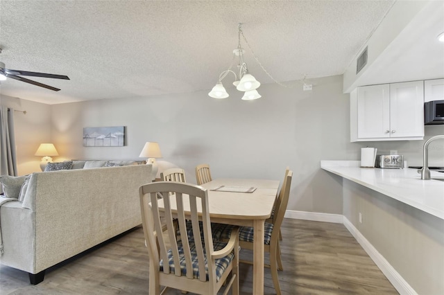 dining space with ceiling fan with notable chandelier, a textured ceiling, dark hardwood / wood-style flooring, and sink