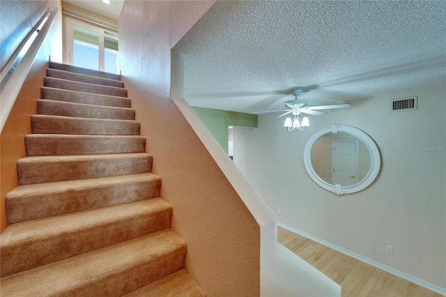 stairway featuring wood-type flooring, a textured ceiling, and ceiling fan