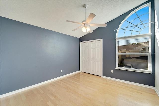 unfurnished bedroom featuring vaulted ceiling, ceiling fan, light wood-type flooring, a textured ceiling, and a closet