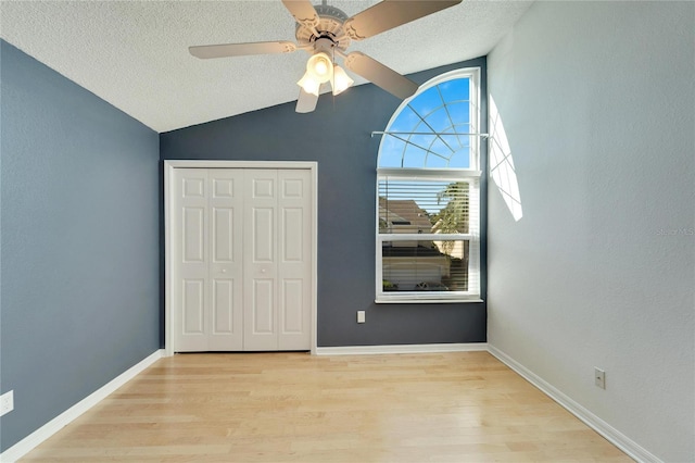 unfurnished bedroom featuring a textured ceiling, ceiling fan, light hardwood / wood-style flooring, a closet, and lofted ceiling