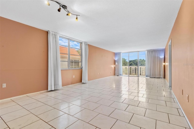 tiled empty room with a wealth of natural light, expansive windows, and a textured ceiling