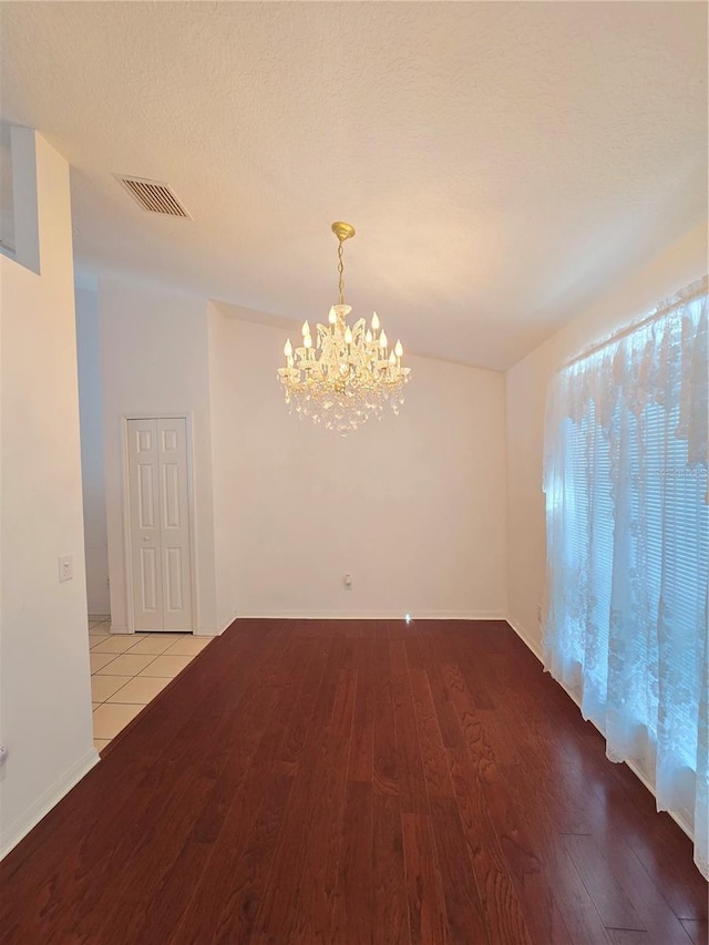 unfurnished room featuring a notable chandelier, light hardwood / wood-style floors, and a textured ceiling