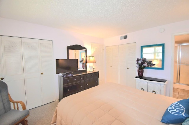 bedroom with a textured ceiling, light carpet, and multiple closets