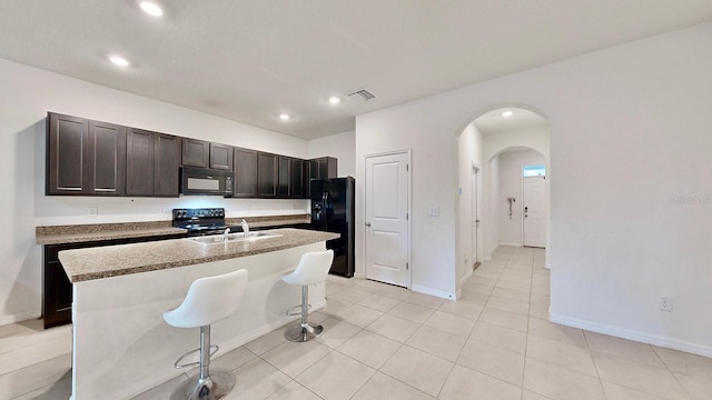 kitchen featuring sink, a kitchen breakfast bar, black appliances, dark brown cabinets, and a kitchen island with sink