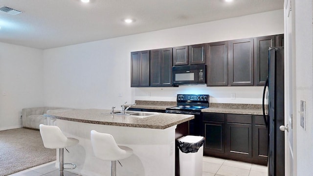 kitchen with light tile patterned floors, black appliances, a kitchen island with sink, a kitchen breakfast bar, and sink