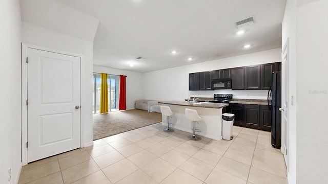 kitchen with sink, a kitchen bar, an island with sink, black appliances, and light colored carpet