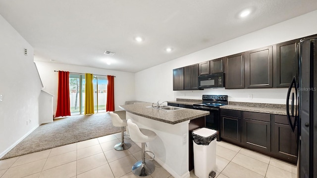 kitchen with sink, a breakfast bar area, a center island with sink, black appliances, and light colored carpet