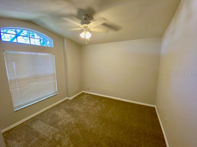 unfurnished room with ceiling fan, dark carpet, and vaulted ceiling