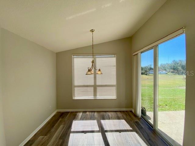 unfurnished dining area featuring a notable chandelier, a healthy amount of sunlight, dark wood-type flooring, and vaulted ceiling