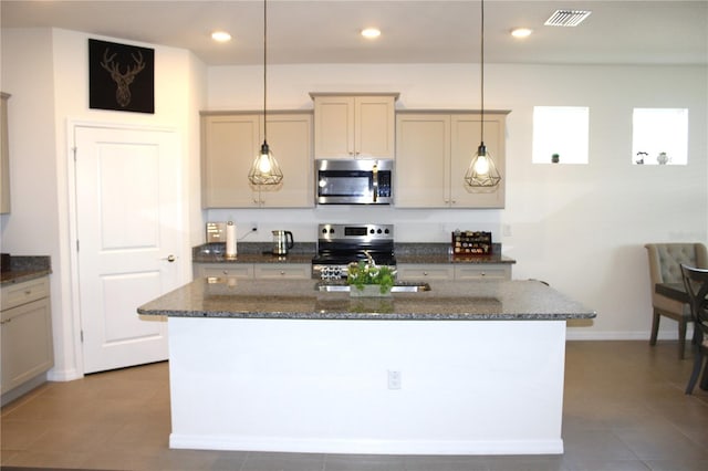 kitchen with hanging light fixtures, tile patterned floors, dark stone countertops, a kitchen island with sink, and appliances with stainless steel finishes