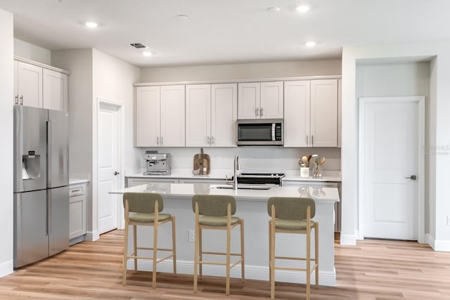 kitchen featuring light wood-style flooring, a kitchen bar, stainless steel appliances, and light countertops