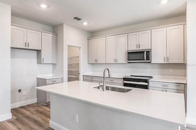 kitchen with a center island with sink, visible vents, stainless steel appliances, light wood-type flooring, and a sink