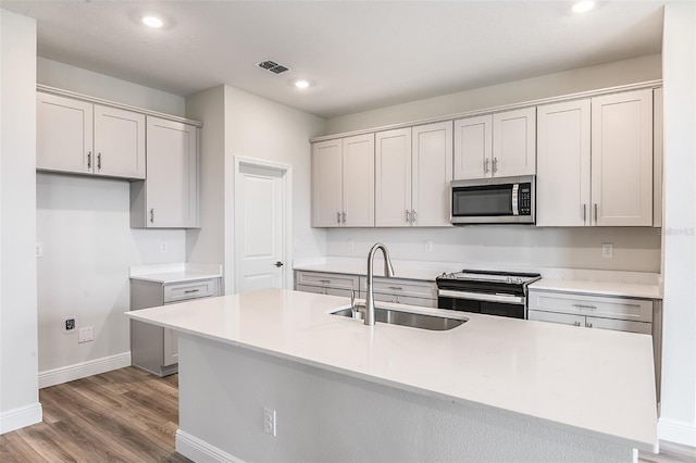 kitchen featuring visible vents, appliances with stainless steel finishes, a sink, wood finished floors, and baseboards