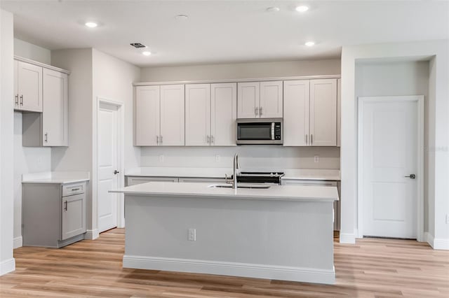 kitchen featuring light countertops, stainless steel microwave, a sink, and light wood-style floors