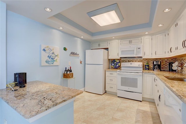 kitchen with a raised ceiling, kitchen peninsula, white cabinets, and white appliances