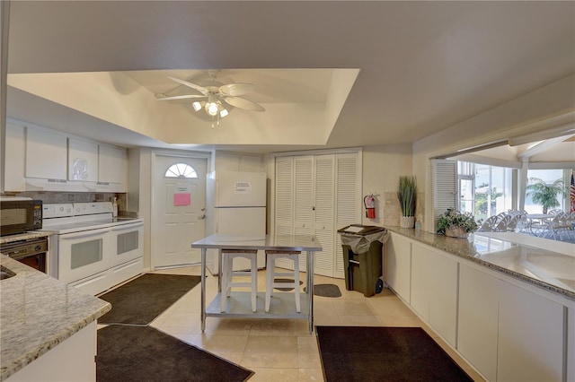 kitchen featuring white cabinetry, ceiling fan, white appliances, a tray ceiling, and light tile patterned floors