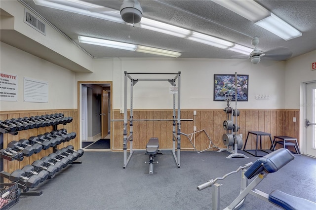 gym featuring ceiling fan, wood walls, and a textured ceiling