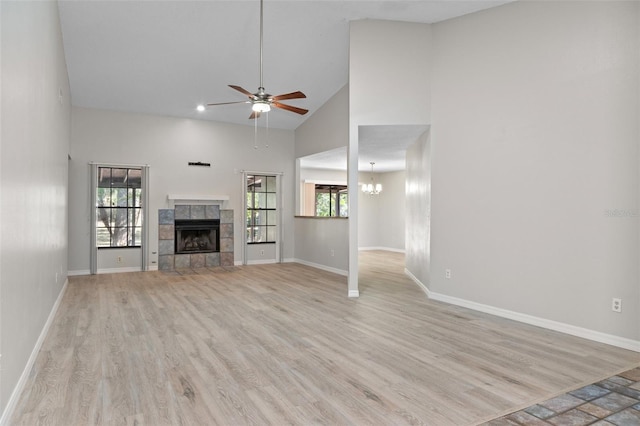 unfurnished living room featuring a tile fireplace, ceiling fan with notable chandelier, light hardwood / wood-style flooring, and high vaulted ceiling