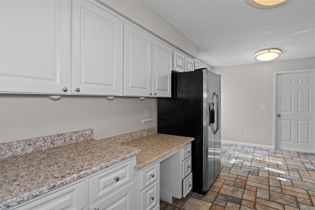 kitchen with white cabinetry, light stone counters, stainless steel fridge with ice dispenser, and a textured ceiling