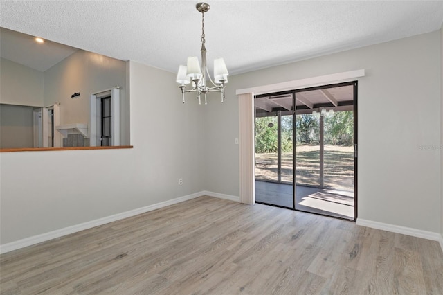 empty room featuring a textured ceiling, an inviting chandelier, vaulted ceiling, and light wood-type flooring