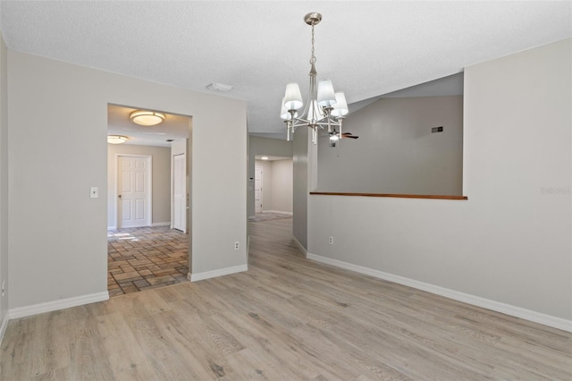 spare room featuring a chandelier, a textured ceiling, and light hardwood / wood-style floors