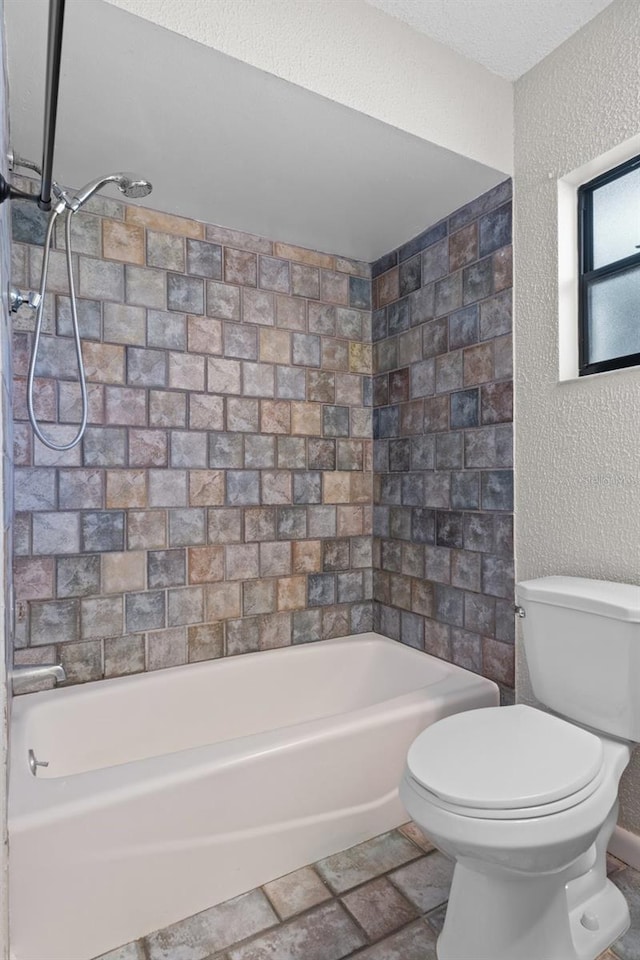 bathroom featuring a textured ceiling, toilet, and tiled shower / bath