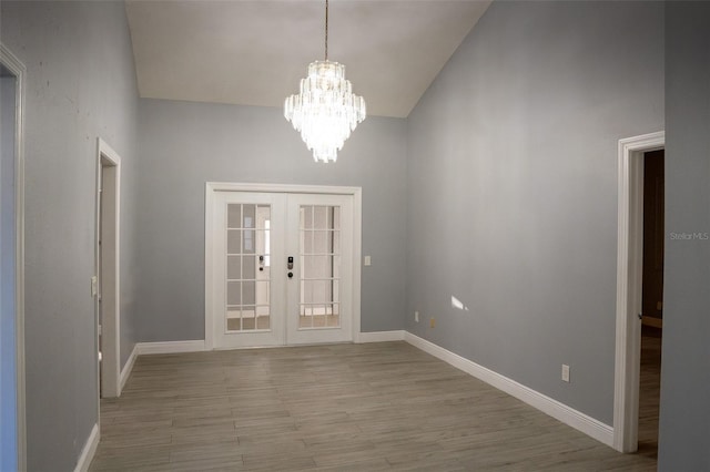 interior space featuring french doors, light wood-type flooring, an inviting chandelier, and a high ceiling