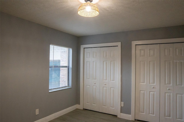 unfurnished bedroom with a textured ceiling, two closets, and light hardwood / wood-style floors