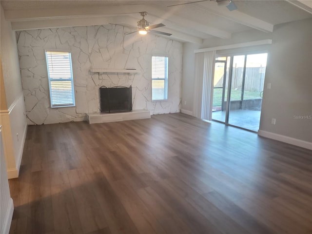 unfurnished living room featuring vaulted ceiling with beams, dark hardwood / wood-style floors, a stone fireplace, and ceiling fan