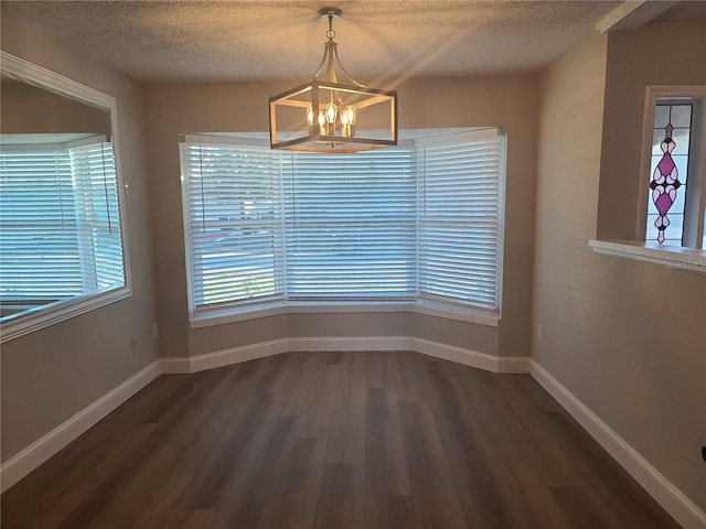 unfurnished dining area with dark hardwood / wood-style flooring, a textured ceiling, and an inviting chandelier