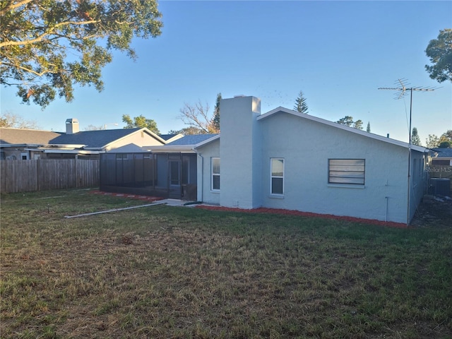 rear view of property with a sunroom, a yard, and central AC