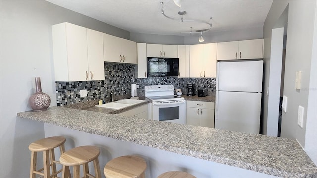 kitchen featuring kitchen peninsula, backsplash, white appliances, sink, and a breakfast bar area