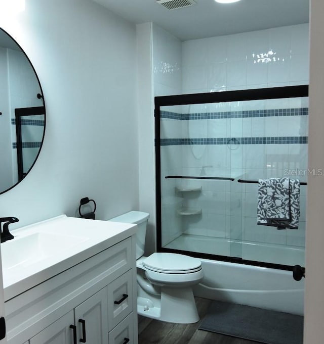 full bathroom with toilet, bath / shower combo with glass door, vanity, and hardwood / wood-style floors