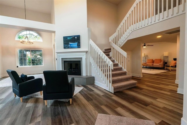 living room featuring a tiled fireplace, ceiling fan, dark hardwood / wood-style flooring, and a towering ceiling