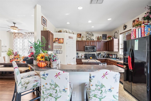 kitchen featuring black appliances, sink, light hardwood / wood-style flooring, ceiling fan, and a kitchen bar