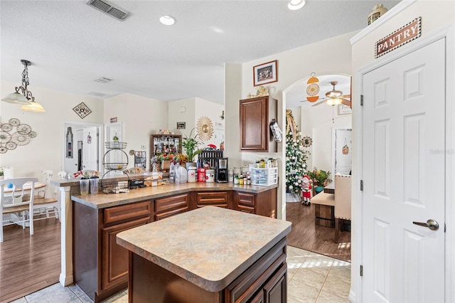 kitchen with a textured ceiling, light hardwood / wood-style floors, kitchen peninsula, and hanging light fixtures