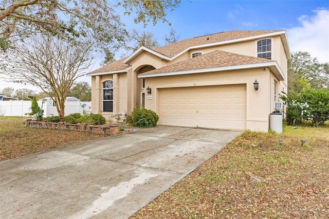 view of front facade featuring concrete driveway, roof with shingles, an attached garage, fence, and stucco siding